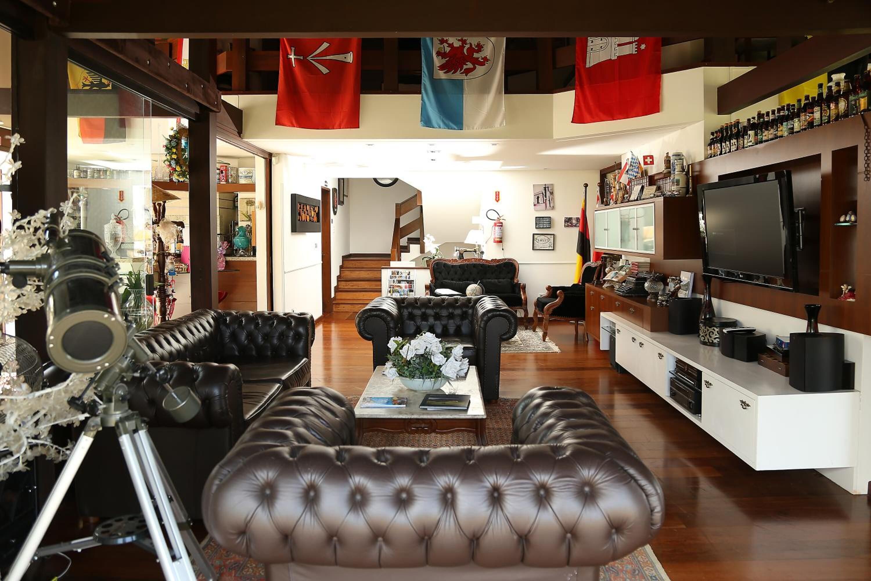 Ein Wohnzimmer mit einer Ledersofa, einem Couchtisch mit Blumen, einem Fernseher und einem Bücherregal.