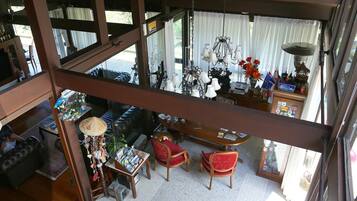 A spacious living area with a high ceiling, large windows, and a view of the outdoors.