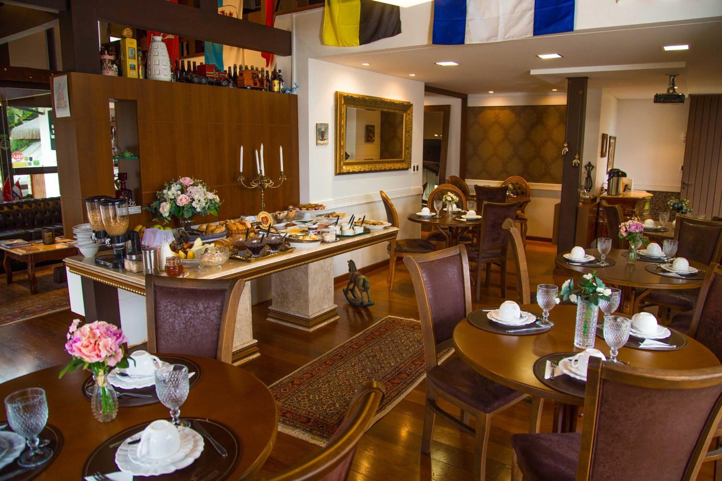 Un restaurante con varias mesas de comedor, cada una dispuesta con platos, vasos y cubiertos. Hay flores decorativas en las mesas, y una zona de bar con botellas y vasos.