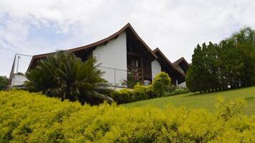 Un edificio moderno con techo inclinado y un balcón, rodeado de abundante vegetación y árboles.