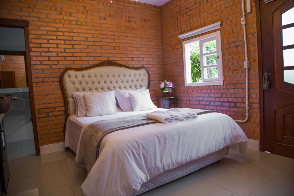 Een slaapkamer met een bakstenen muur, een groot bed met witte beddengoed, een raam en een houten deur.