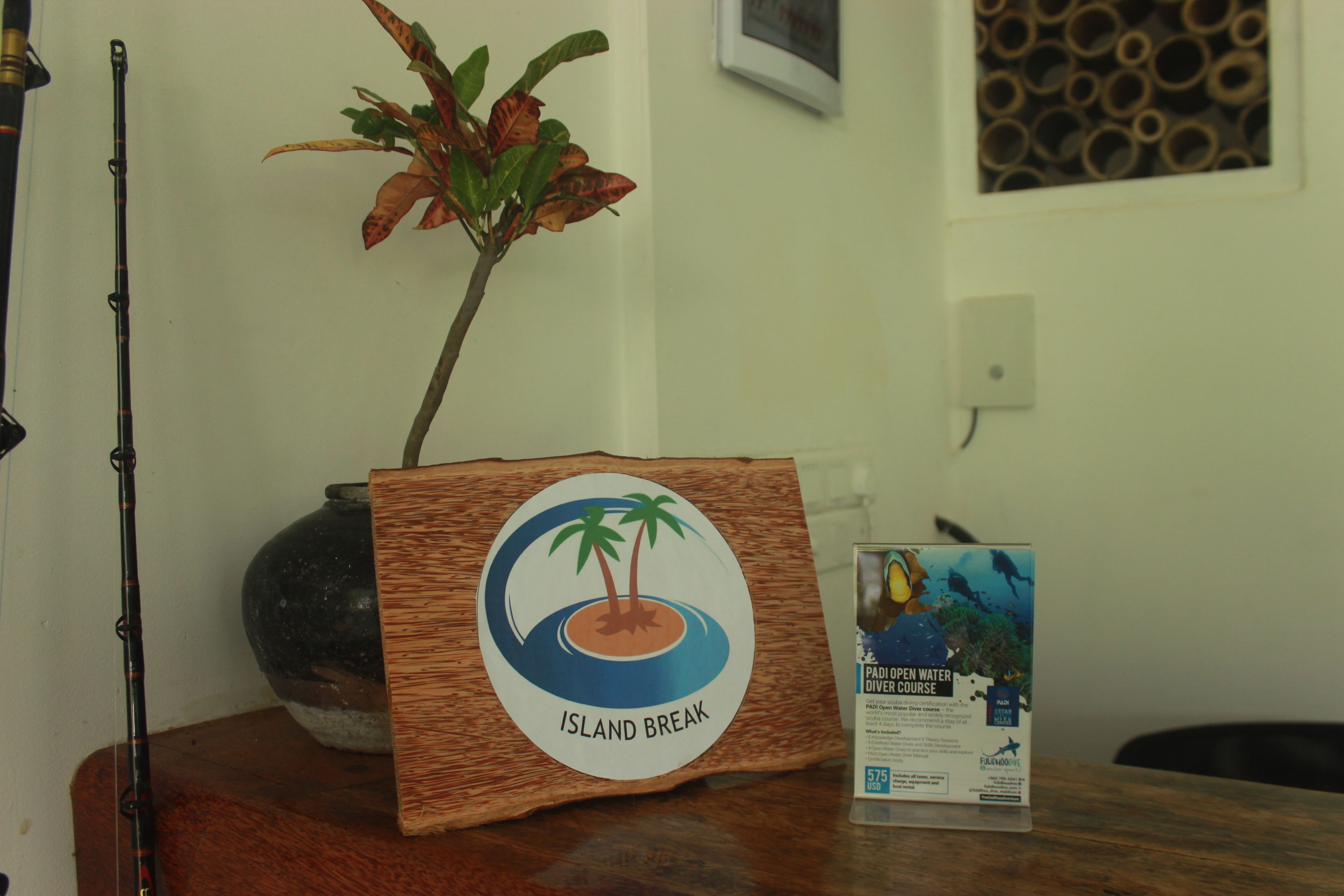A wooden sign with a palm tree and island logo labeled "Island Break" on a table, next to a fishing rod and a brochure.