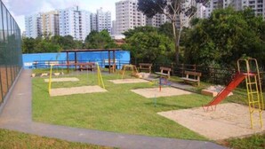 A playground with swings, slides, and benches, surrounded by a grassy area and trees, with high-rise buildings in the background. - Golden Dolphin Grand Hotel - Apartamento (Caldas Novas)