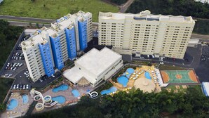 A high-rise hotel with multiple floors, a swimming pool area, and a tennis court. - Golden Dolphin Grand Hotel - Apartamento (Caldas Novas)