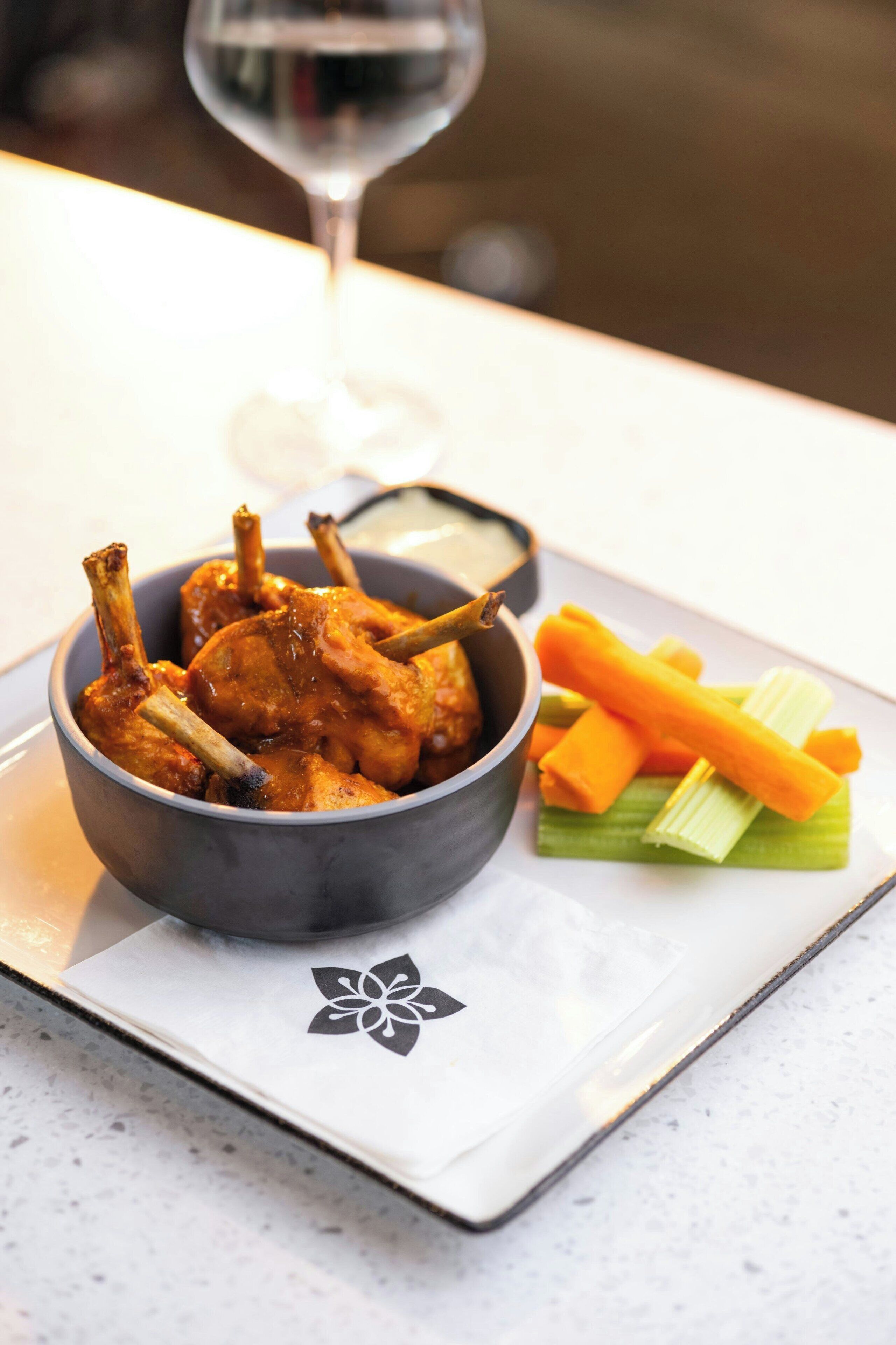 Ein Teller mit gegrillten Chicken Wings, Sellerie und Karottenstiften, dazu ein Glas Wein.