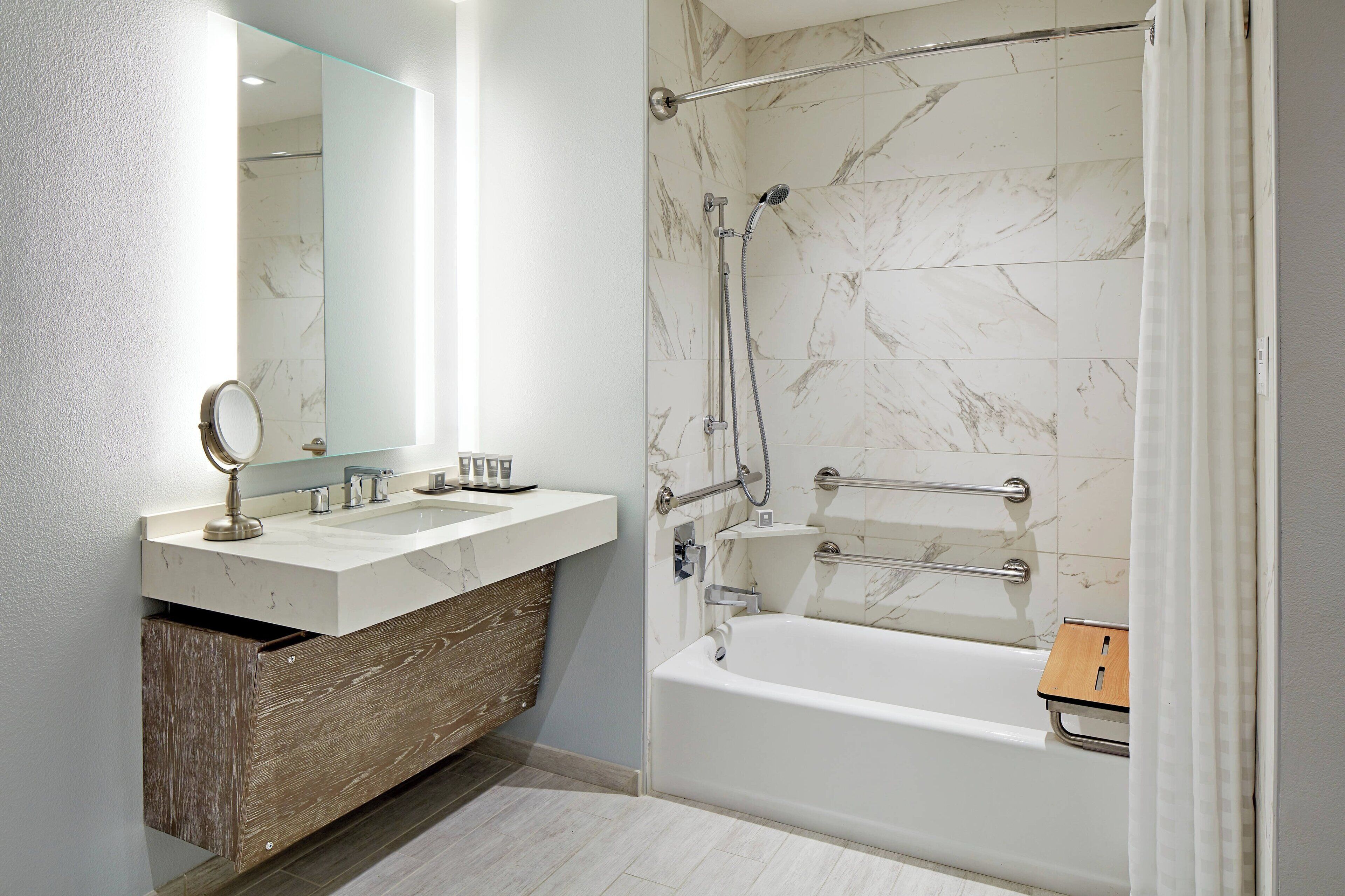 A modern bathroom with a marble shower, a wooden vanity, and a bathtub.