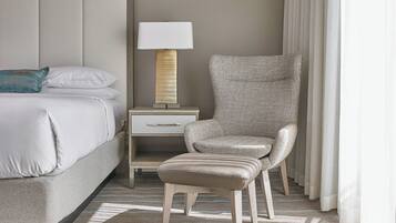 A hotel room with a bed, a nightstand, a lamp, a chair, and a window with curtains.