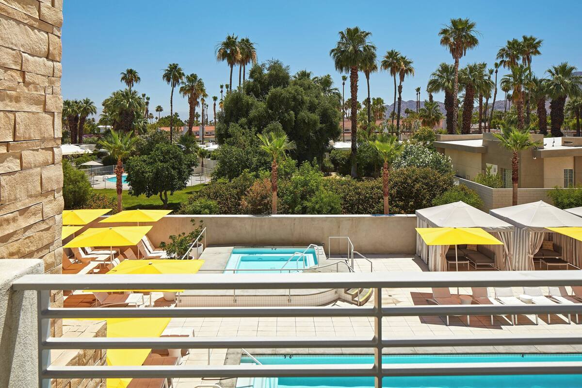 A rooftop pool area with yellow umbrellas, lounge chairs, and a clear view of palm trees and buildings in the background.