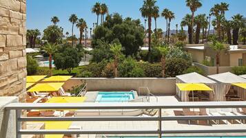 Un espace piscine aménagé sur le toit, avec des parasols jaunes, des chaises longues et une vue dégagée sur les palmiers et les bâtiments en arrière-plan.
