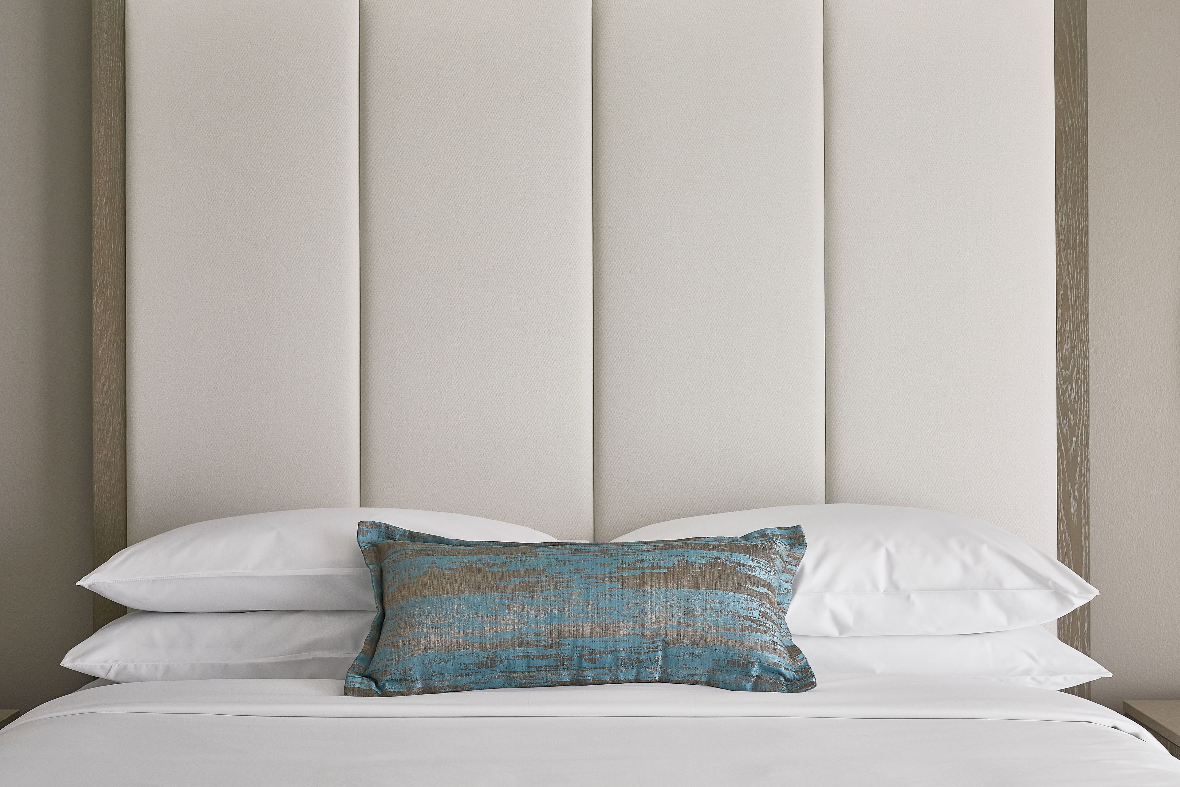 A bed with white bedding and a single decorative pillow.