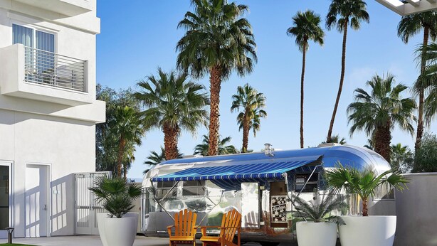 A modern house with a large white exterior, a covered outdoor area with two wooden chairs, and several potted plants. - Hotel Paseo, Autograph Collection by Marriott (Palm Desert)