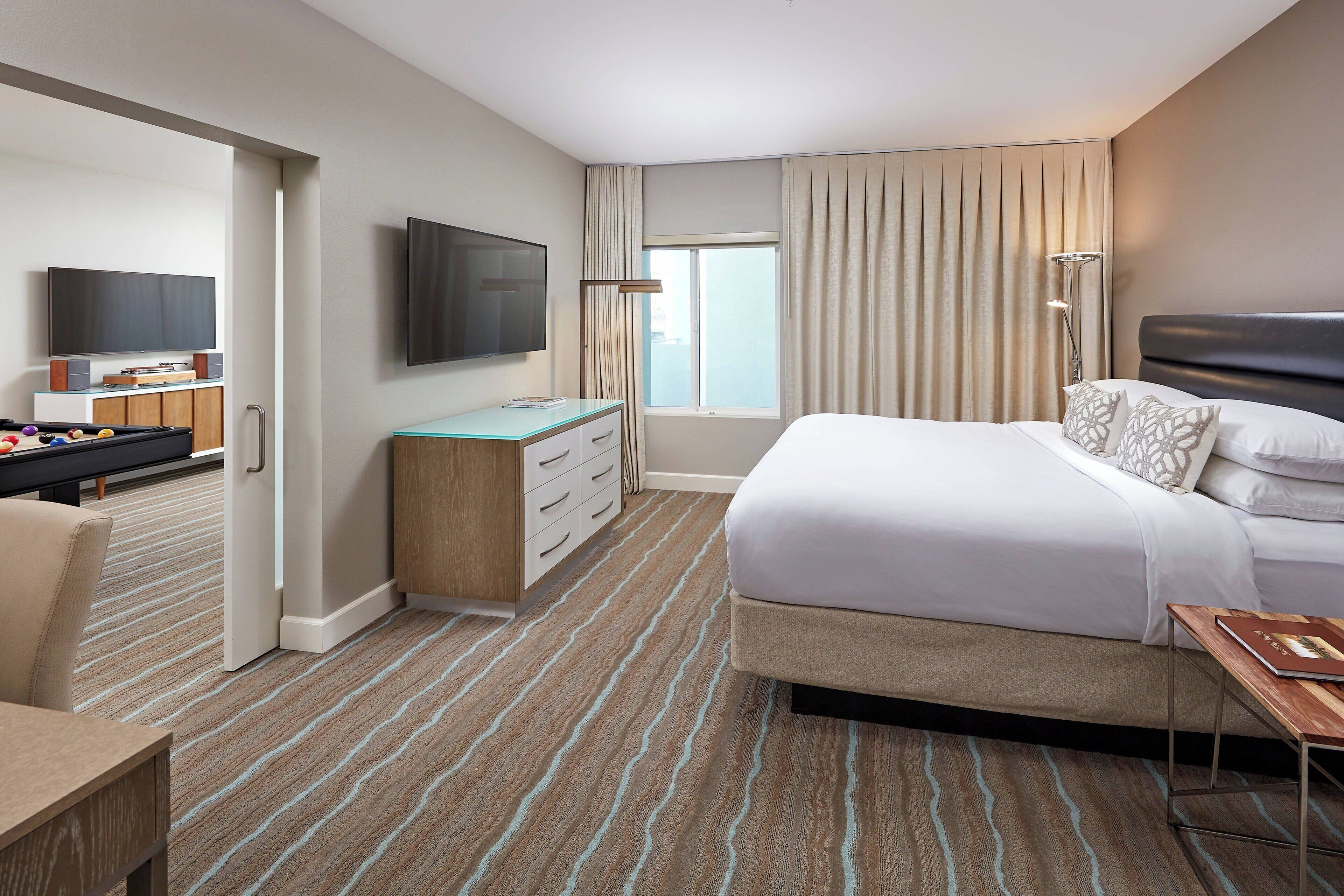 A hotel room with a bed, a desk, a television, and a window with curtains.