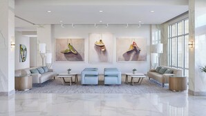 A spacious lobby with a marble floor, a sofa, two ottomans, a coffee table, and artwork on the walls. - Hotel Paseo, Autograph Collection by Marriott (Palm Desert)