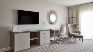 Habitación de hotel con televisor de pantalla plana, espejo redondo, escritorio con silla y ventana grande con cortinas.