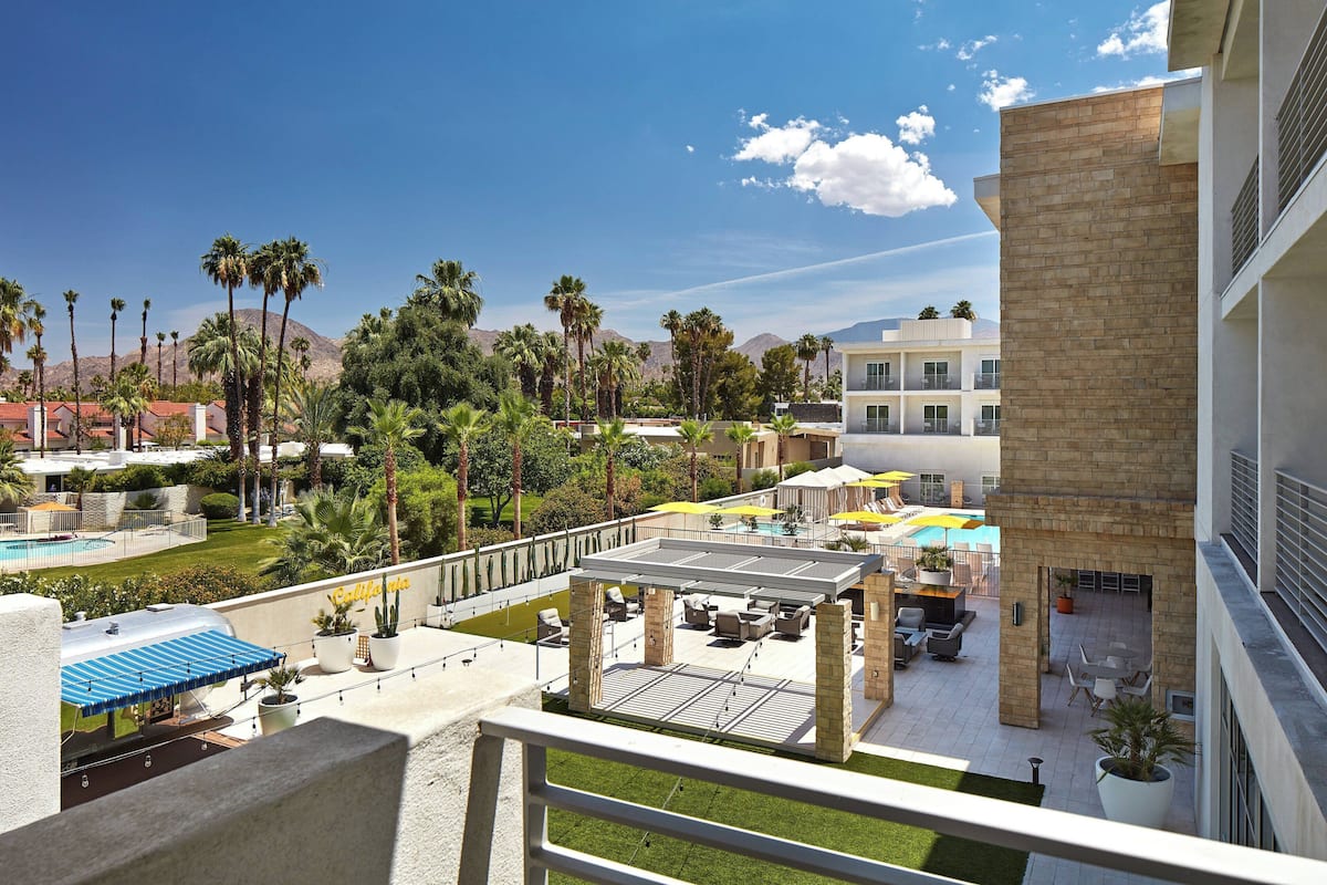 A hotel courtyard with a pool, outdoor seating, and palm trees.