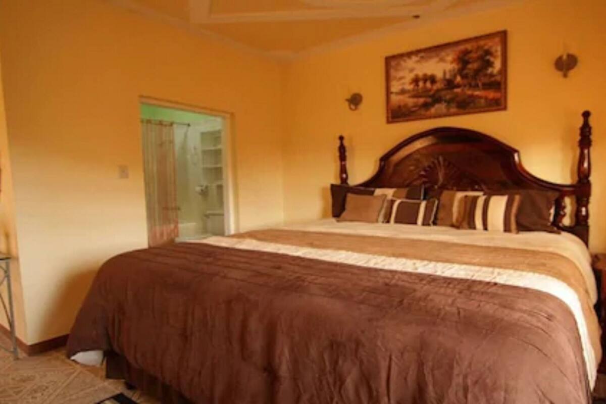 A bedroom with a large bed, a wooden headboard, a painting on the wall, and a door leading to a bathroom.