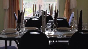 A dining table set for four with chairs, a view of greenery outside through a window, and curtains on either side. - Paradise Reggae Resort (Spanish Town)