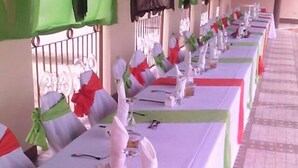 A row of tables set for a formal event, each with a white tablecloth, red napkins, and silverware. - Paradise Reggae Resort (Spanish Town)