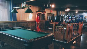 A pool table in a dimly lit room with wooden walls and a bar area with multiple slot machines. - Hi Valley Motor Inn (Valleyview)