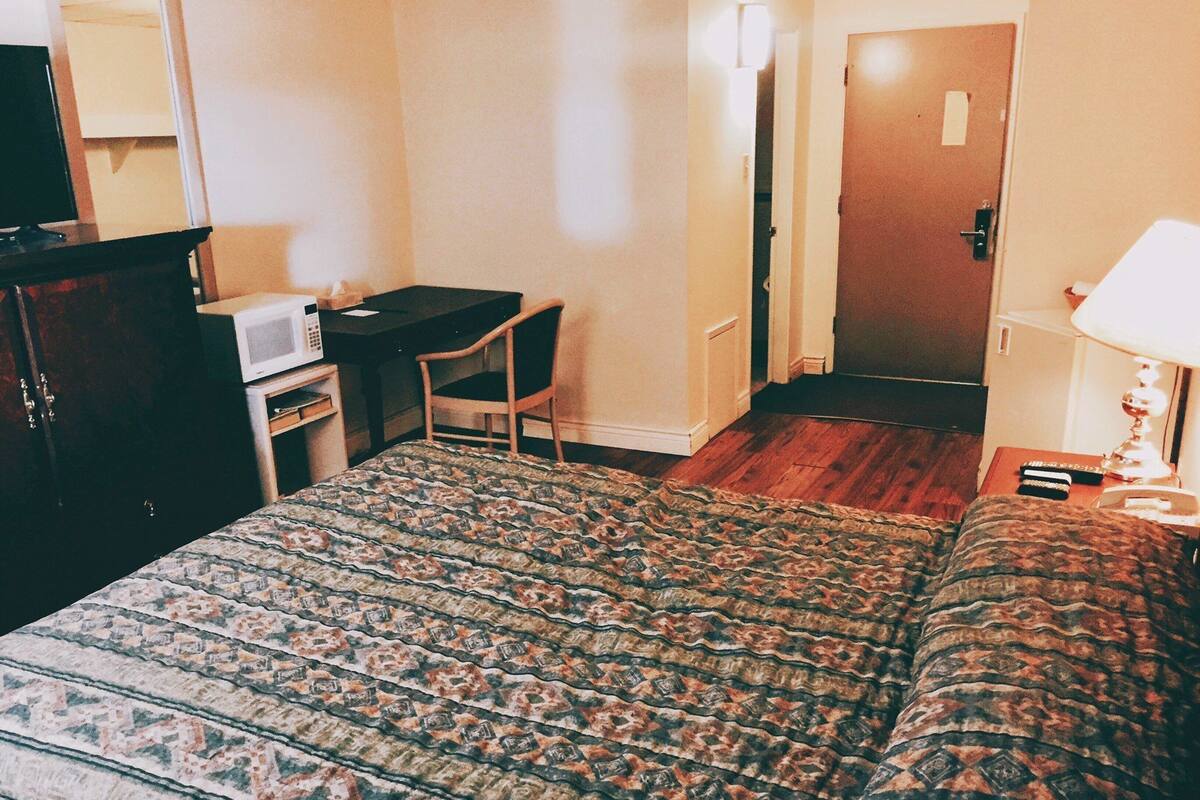 A hotel room with a bed, a desk, a chair, a microwave, and a door leading to another room.