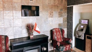 A lobby with a stone wall, a clock, a flat-screen TV, a patterned armchair, a fireplace, and an ATM. - Hi Valley Motor Inn (Valleyview)