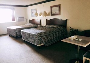 A room with two beds, a small table, and a chair. There is a window with curtains, a wall-mounted air conditioner, and two wall-mounted lamps. - Hi Valley Motor Inn (Valleyview)