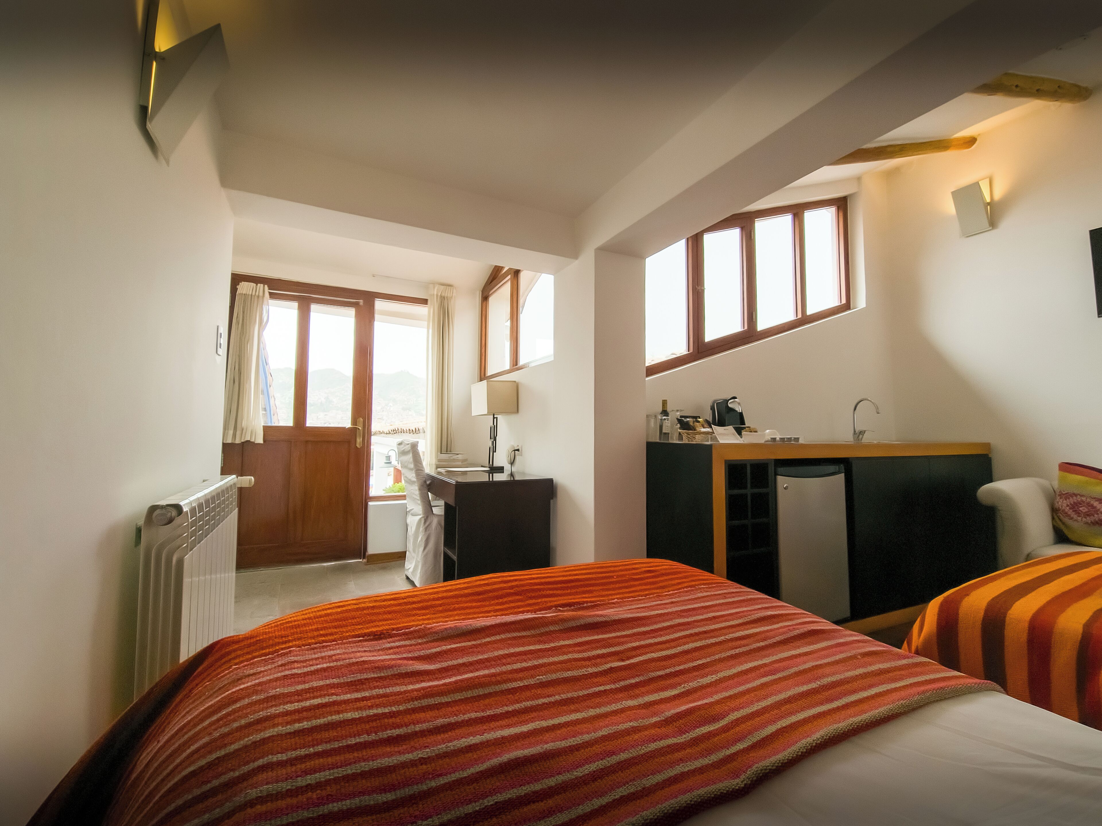 A bedroom with a bed, a desk, a chair, a radiator, a window, and a view of the outdoors.