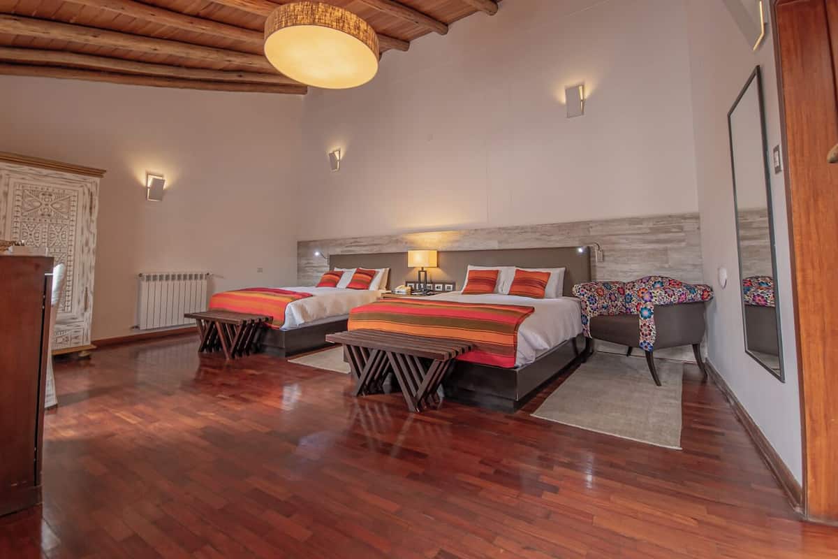 Une chambre d’hôtel avec deux lits, un plancher en bois, un grand lustre et un plafond en bois.