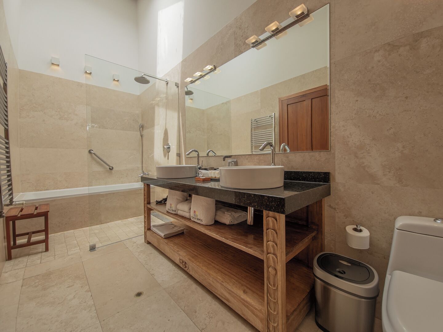Un baño moderno con lavamanos doble, un espejo grande, ducha y tocador de madera.
