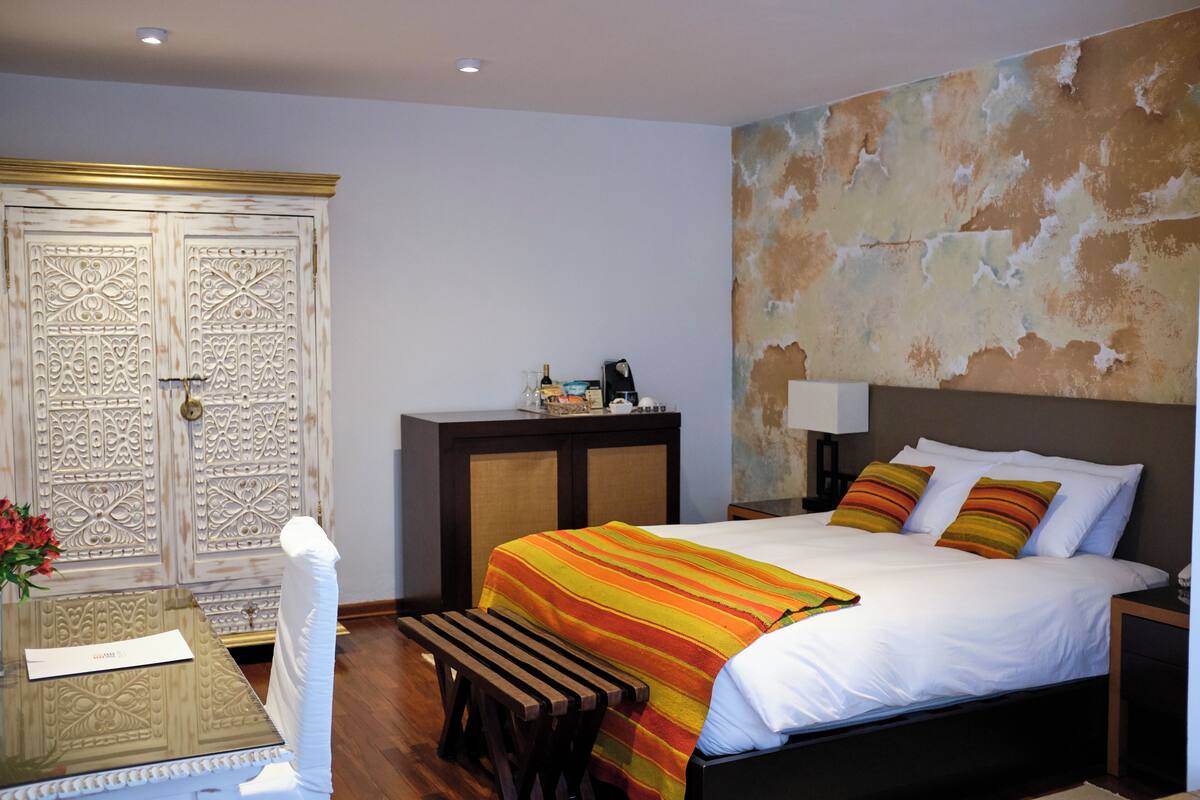 Une chambre d’hôtel avec un lit, un bureau, une chaise, une armoire et un mur dont la peinture s’écaille.