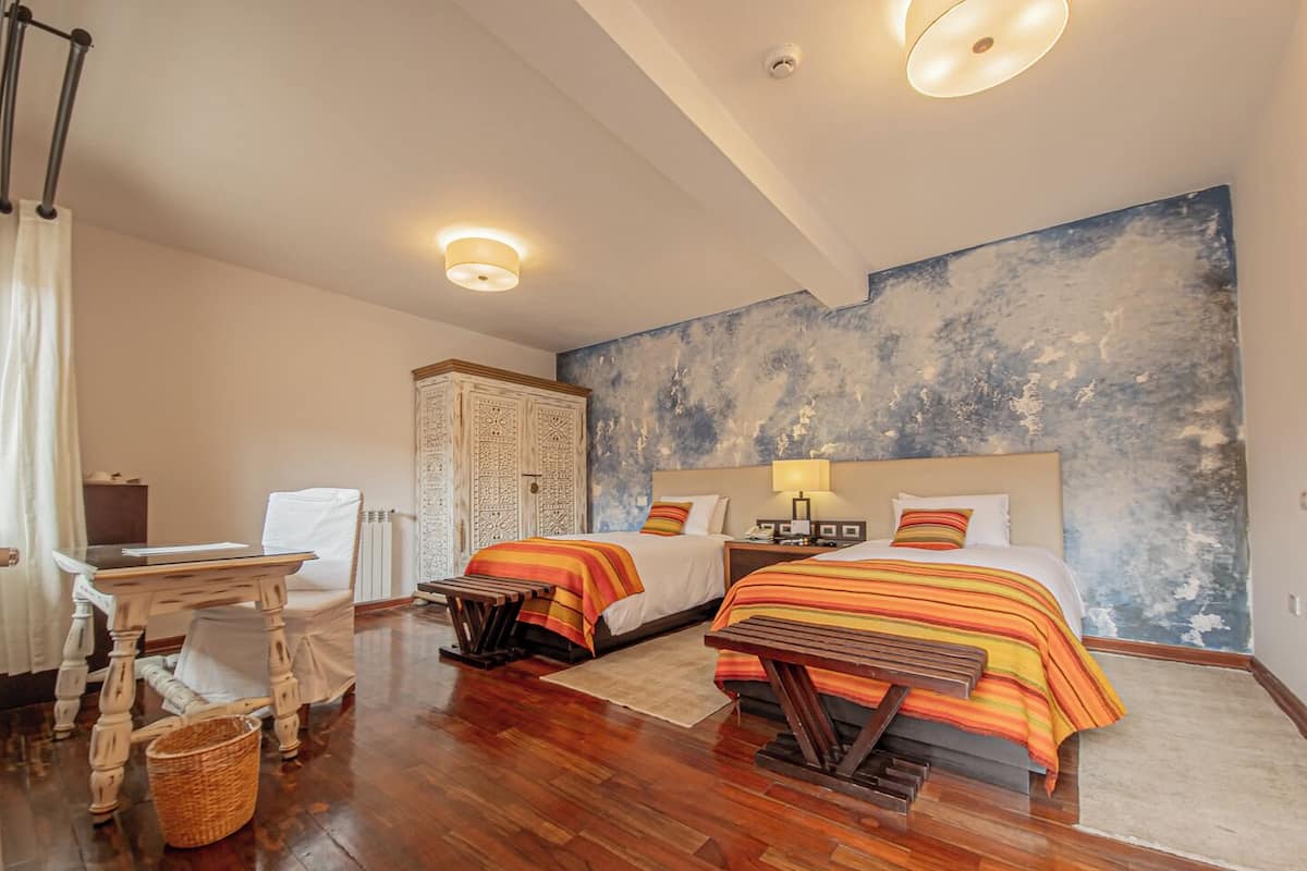 Une chambre d’hôtel avec deux lits, un bureau, une chaise, une armoire et un grand tableau abstrait accroché au mur.