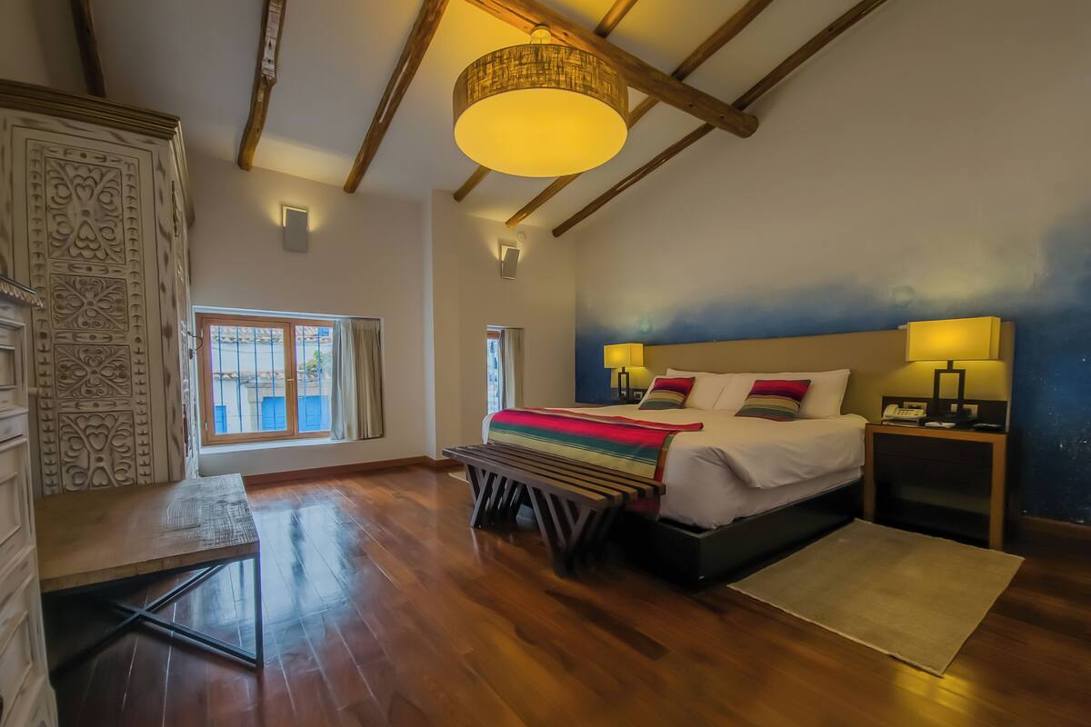Une chambre à coucher avec un lit, des tables de chevet, un banc en bois, un mur à motifs et une fenêtre.
