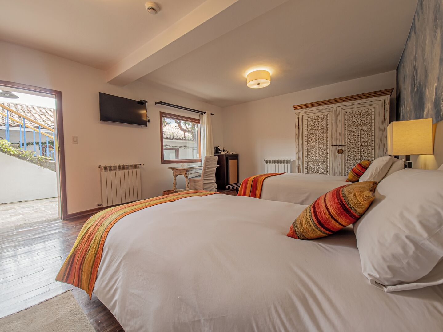 A bedroom with two beds, a TV, a desk, and a door with intricate patterns.