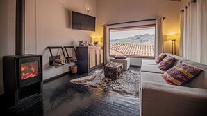 Una sala de estar acogedora con chimenea, televisor, sofá con cojines estampados y vistas a un paisaje urbano a través de un ventanal grande.