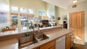 A kitchen with a double sink, wooden cabinets, and a dishwasher. There are windows with views of a snowy landscape.