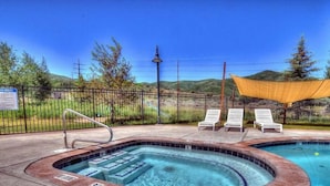 A hot tub with a pool, surrounded by a fence, with a mountain view in the background.