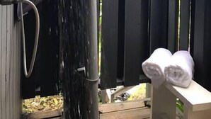 En træterrasse med gelænder i sort, et vandelement og en håndklædestang med håndklæder.