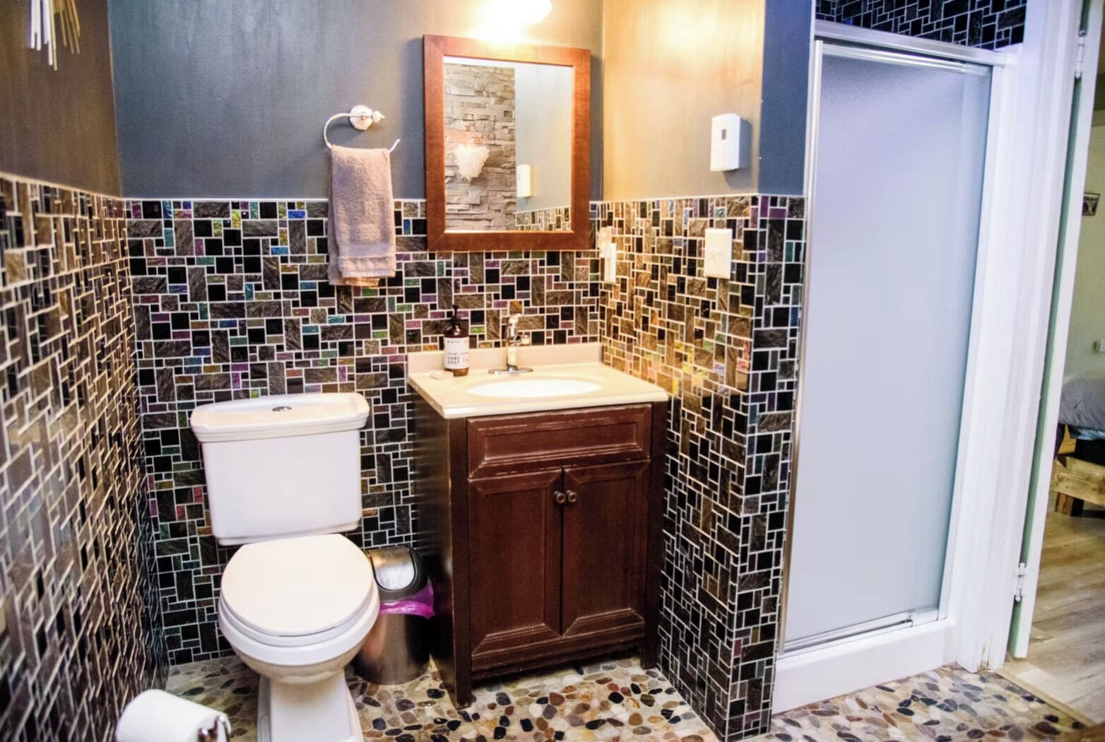 Un bagno con WC, lavandino e specchio. Le pareti sono rivestite da un motivo a mosaico.