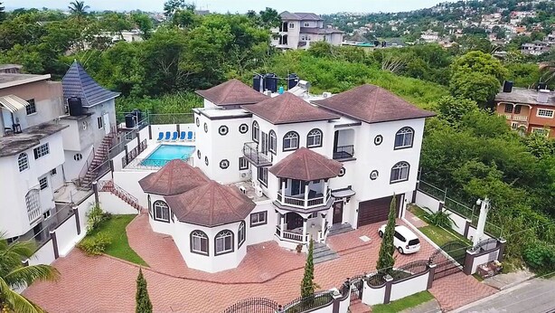 Une grande maison à plusieurs étages, dotée d’une piscine, entourée d’une végétation luxuriante et d’autres immeubles résidentiels.