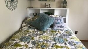 A bedroom with a floral bedspread, a blue pillow, a wall-mounted fan, and a painting above the bed. - Tomar Park Apt 2 - KP101APT2 (Sioux Falls)