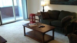 A living room with a dark wooden coffee table, a green sofa, a red lantern, and a lamp on a side table. - Tomar Park Apt 2 - KP101APT2 (Sioux Falls)