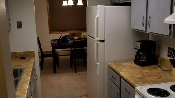 A compact kitchen with a refrigerator, stove, and a dining area with a table and chairs. - Tomar Park Apt 2 - KP101APT2 (Sioux Falls)