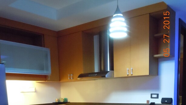 A compact kitchen with wooden cabinets, a built-in oven, a sink, and a bar stool. - First Class Apartment, Best kept Secret in Angeles City ! 
Perfect location! (Angeles City)