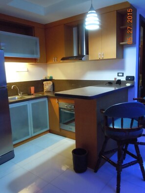 A compact kitchen with wooden cabinets, a built-in oven, a sink, and a bar stool.