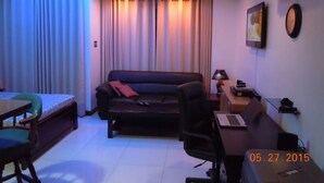 A compact hotel room with a bed, a sofa, a desk with a laptop, a chair, and an air conditioning unit. - First Class Apartment, Best kept Secret in Angeles City ! 
Perfect location! (Angeles City)