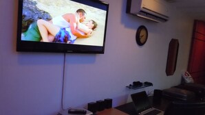 A living room with a flat-screen TV mounted on the wall, a clock, a laptop, and a speaker on a table. - First Class Apartment, Best kept Secret in Angeles City ! 
Perfect location! (Angeles City)