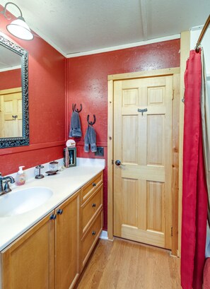 A bathroom with wooden cabinets, a white sink, a mirror, and a red shower curtain.