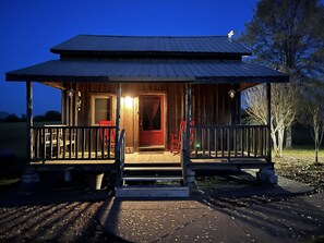 A wooden cabin with a porch, a red door, and a small outdoor seating area.