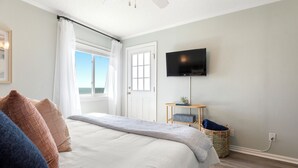 A bedroom with a bed, a television on the wall, a window with curtains, and a view of the outdoors. - Beautiful Top Floor Oceanfront Condo, Breathtaking Views from
Oceanfront Balcony (Carolina Beach)