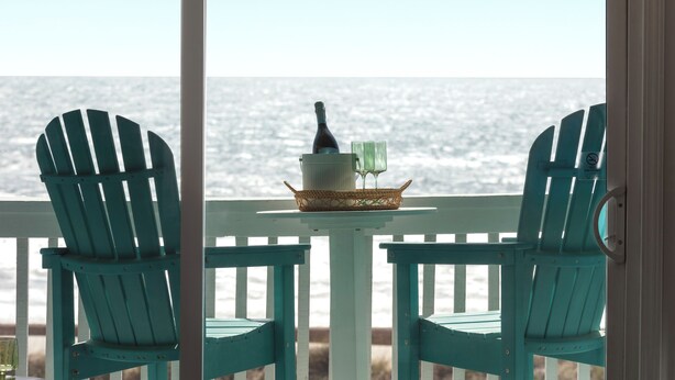 A view from a balcony with two turquoise Adirondack chairs, a small table with a bottle and glasses, and a wicker basket. - Beautiful Top Floor Oceanfront Condo, Breathtaking Views from
Oceanfront Balcony (Carolina Beach)